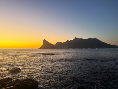 Die untergehende Sonne taucht den Himmel in warme Gelbtöne über dem ruhigen Wasser von Hout Bay.