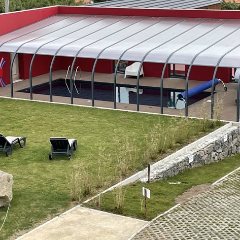 Ein moderner Poolbereich mit einem überdachten Schwimmbad, umgeben von grünem Rasen und zwei Liegen zum Entspannen.