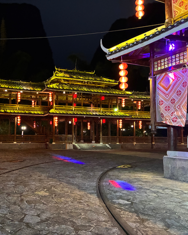 Eine malerische Nachtansicht eines traditionellen Gebäudes, beleuchtet von roten Laternen und bunten Lichtern auf dem Boden.