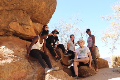 Eine Reisegruppe sitzt gemeinsam im Schatten eines Felsens an der Spitzkoppe - Namibia mit Kindern