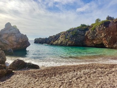 Eine ruhige Bucht mit klarem, türkisfarbenem Wasser, umgeben von steilen Felsen und sanften Wellen am Strand.