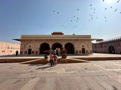 Eine Gruppe von Besuchern geht auf eine große, kunstvoll gestaltete Terrasse des Stadtpalasts in Jaipur zu.