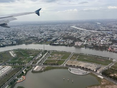 Der Blick aus dem Flugzeug zeigt eine weitläufige Stadtlandschaft mit einem Fluss, der sich durch die grüne Umgebung schlängelt.
