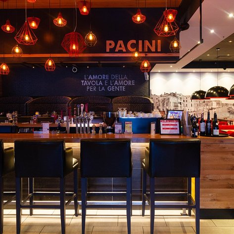 Ein stilvolles Restaurant mit einer langen Bar, umgeben von roten Pendelleuchten und eleganten Sitzbereichen im Hintergrund.
