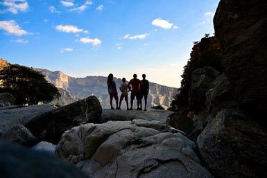 Eine Familie steht am Rand der Schlucht und bewundert die spektakuläre Berglandschaft des Jebel Shams – Oman Familienreise
