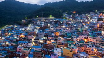 Die bunten Häuser des Gamcheon Culture Village leuchten in der Dämmerung, umgeben von sanften Hügeln und einem klaren Himmel.