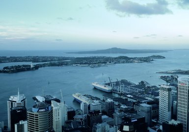 Ein Blick auf den Hafen von Auckland, mit Segelbooten und großen Frachtschiffen im Wasser, umgeben von modernen Gebäuden.