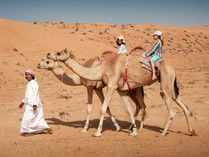 Beduine führt zwei Kamele mit zwei Mädchen durch die Wüste – Oman Familienreise