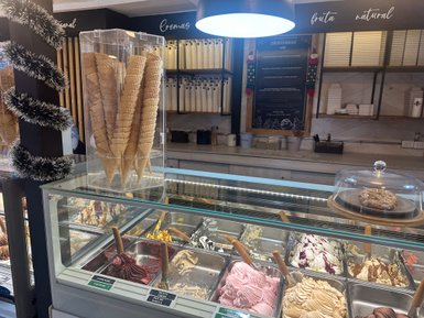 Eine Eisdiele mit einer Auswahl an buntem Eis in verschiedenen Behältern und einem klaren Display für Waffeln im Vordergrund.