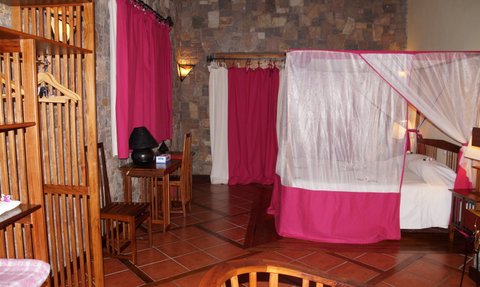 Ein gemütliches Zimmer mit Steinwänden, pinken Vorhängen und einem Himmelbett, das eine entspannende Atmosphäre schafft.