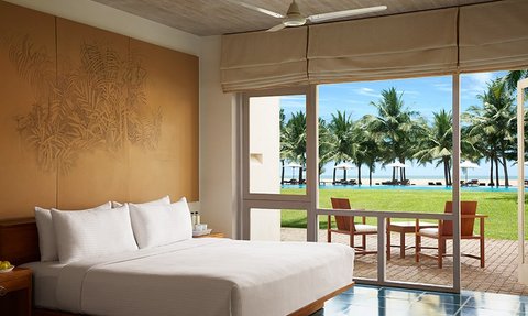 Ein helles Hotelzimmer mit einem großen Fenster, das auf einen tropischen Garten und den Strand blickt.