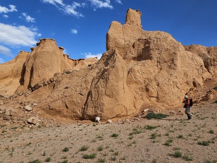 Ein Wanderer erkundet die beeindruckenden, sandfarbenen Felsformationen unter einem strahlend blauen Himmel in der Mongolei.
