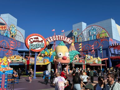 Bunte Attraktionen und fröhliche Menschenmengen im Krustyland von Universal Studios Hollywood unter strahlend blauem Himmel.