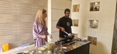 Eine blonde Frau und ein Mann kochen gemeinsam in einer modernen Küche, umgeben von verschiedenen Zutaten und Kochgeschirr.