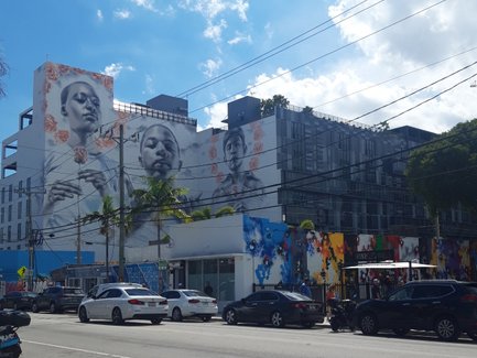 Eine lebendige Straßenszene in Wynwood, Miami, mit beeindruckenden Wandmalereien und blauen Himmel im Hintergrund.