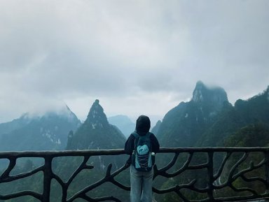 Eine Frau mit einem Rucksack steht an einem Aussichtspunkt und blickt auf die nebligen Berge von Tianmen.