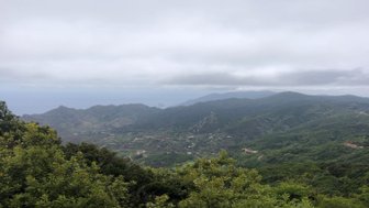 Eine weite Aussicht auf grüne Berge und Hügel, die unter einem bewölkten Himmel liegen, mit dem Ozean in der Ferne.