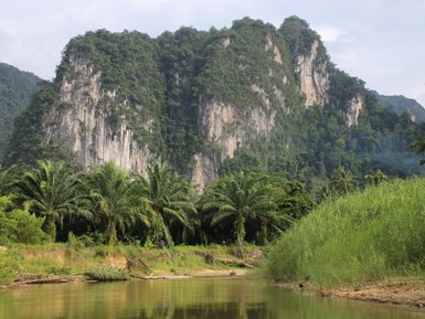 Ein ruhiger Fluss schlängelt sich durch eine üppige Landschaft, umgeben von hohen Bergen und dichten Wäldern.