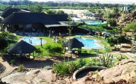 Eine weitläufige Anlage mit mehreren Schwimmbecken, umgeben von grüner Vegetation und Felsen im Hintergrund.