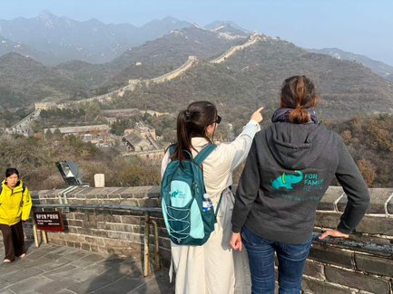 Zwei Frauen stehen auf der Chinesischen Mauer und zeigen auf die beeindruckende Landschaft der Berge im Hintergrund.