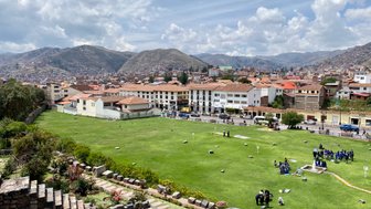 Eine weite Aussicht auf Cusco mit grünen Wiesen, historischen Gebäuden und den majestätischen Anden im Hintergrund.