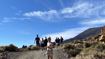 Ein Mädchen in einem weißen T-Shirt und Shorts läuft fröhlich auf einem Wanderweg, umgeben von einer Gruppe von Menschen.