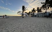 Ein ruhiger Strand mit feinem Sand, umgeben von Palmen und einem malerischen Sonnenuntergang am Horizont.