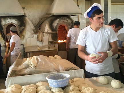 In einer Bäckerei in Taschkent formen Arbeiter Teigstücke, während im Hintergrund Holzöfen brennen.