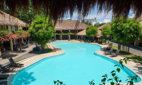 Ein einladender Pool mit klarem Wasser, umgeben von tropischen Pflanzen und gemütlichen Liegen in einem Resort.