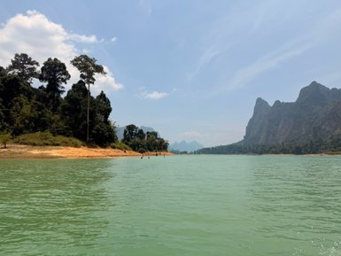 Ein ruhiger See mit grünem Wasser, umgeben von üppigen Bäumen und majestätischen Bergen im Hintergrund.