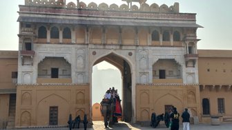 Ein majestätisches Tor des Amber Fort in Jaipur, durch das ein Elefant mit Passagieren schreitet, umgeben von historischen Gebäuden.