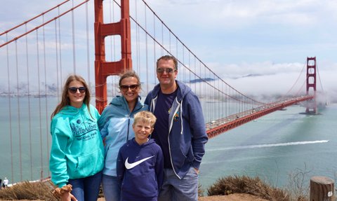 Eine Familie posiert fröhlich vor der Golden Gate Bridge, umgeben von einer malerischen Küstenlandschaft und sanften Wolken.