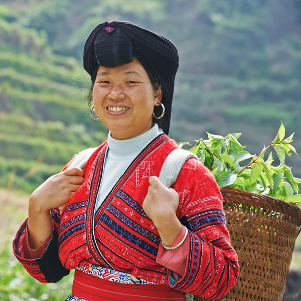 Einheimische Frau der Yao-Minderheit mit traditioneller Kleidung lächelt in die Kamera vor den Reisterrassen von Longsheng – China Familienreise