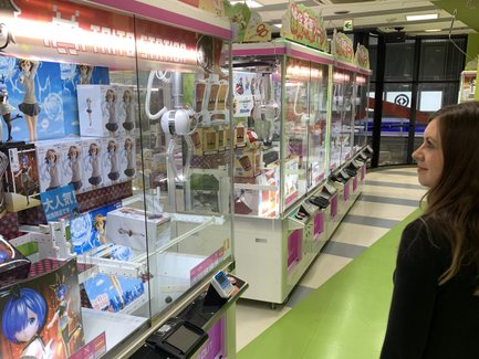 Eine Frau steht vor einer Reihe von Spielautomaten in einem hellen, bunten Raum voller Spielzeugpreise.