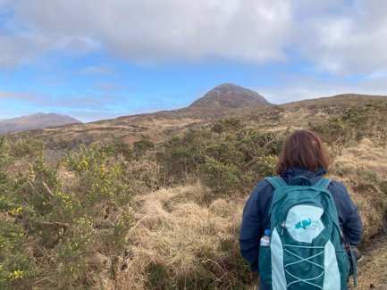 Eine Person mit einem Rucksack steht auf einem Wanderweg und blickt auf den majestätischen Diamond Hill in Irland.
