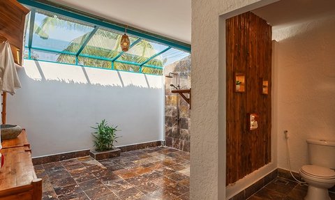 Ein modernes Badezimmer mit einer offenen Dusche, umgeben von Natur und einem großen Fenster, das Tageslicht hereinlässt.