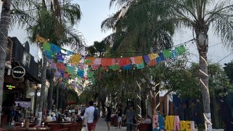 Eine belebte Straße in Playa del Carmen, geschmückt mit bunten Papiergirlanden und umgeben von Palmen.