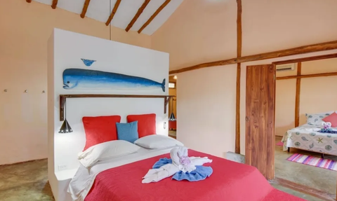 Ein gemütliches Schlafzimmer mit einem roten Bett und einer blauen Wandmalerei eines Fisches über dem Kopfteil.