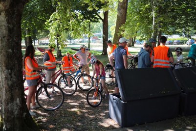Eine Gruppe von Radfahrern in leuchtenden Westen versammelt sich unter Bäumen, während sie ihre Fahrräder überprüfen.