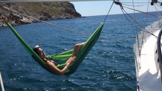 Eine Frau entspannt in einer grünen Hängematte auf einem Segelboot, umgeben von klarem Wasser und sonnigem Himmel.