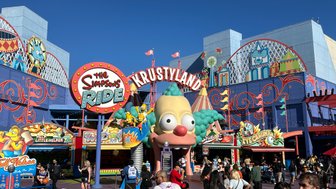 Bunte Attraktionen und fröhliche Menschenmengen im Krustyland von Universal Studios Hollywood unter strahlend blauem Himmel.
