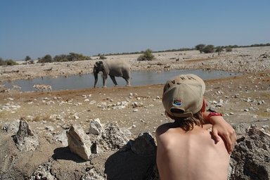 Ein Junge beobachtet gespannt einen Elefant am Wasserloch - Namibia mit Jugendlichen