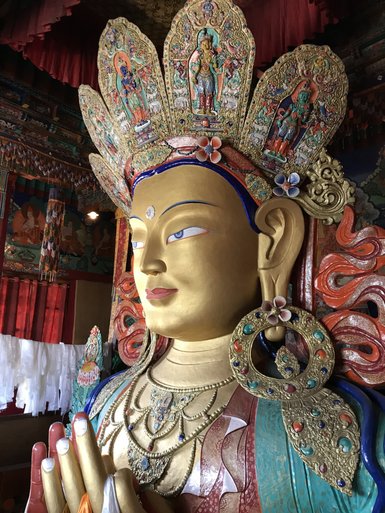 Eine majestätische Statue des Maitreya-Buddha mit kunstvoll verzierten Ohrringen und einem strahlenden Gesichtsausdruck.