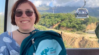 Eine Frau mit Sonnenbrille lächelt in einer Seilbahn, während sie die grüne Landschaft im Hintergrund betrachtet.