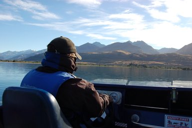 Ein Bootsfahrer steuert ein Jetboot auf dem ruhigen Dart River, umgeben von majestätischen Bergen und klarem Himmel.