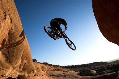 Ein Mountainbiker springt über eine Felsformation, während die Sonne am Horizont aufgeht und den Himmel erleuchtet.