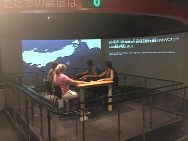 Eine Gruppe von vier Personen sitzt an einem Tisch und interagiert mit einer Projektion einer Karte von Japan.
