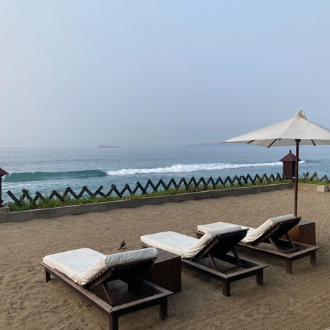 Drei Liegen stehen am Strand, umgeben von feinem Sand, mit Blick auf das ruhige Meer und sanfte Wellen im Hintergrund.