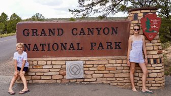 Ein Junge und ein Mädchen posieren lächelnd vor dem Eingangsschild des Grand Canyon Nationalparks.