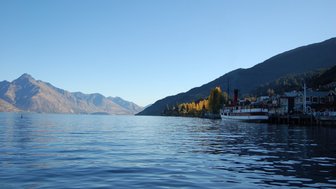 Ein historisches Dampfschiff liegt am Ufer des Lake Wakatipu, umgeben von majestätischen Bergen und bunten Bäumen.